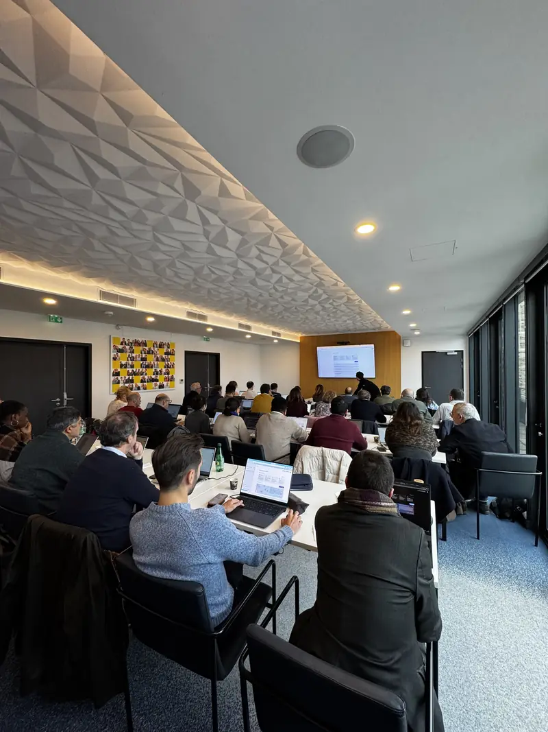 Une salle de formation en longues tables : les participants à leurs ordinateurs, l'écran au fond de la salle.